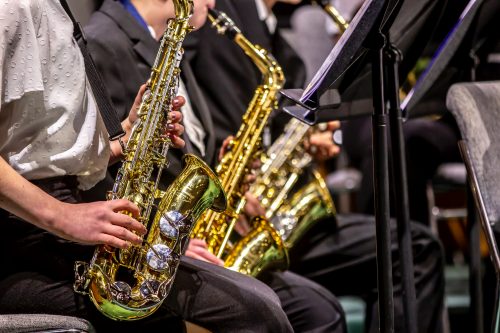 A close up image of three people each playing saxophone. They have light skin and are smartly dressed.