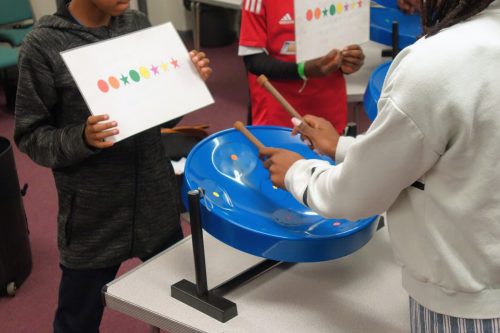 child playing steel pans and other child holding up directions